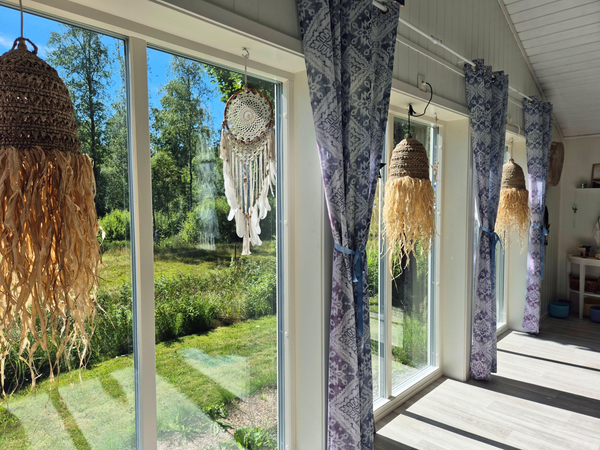 Inomhusveranda med stora fönster, blåmönstrade gardiner och flera drömfångare i bohemisk stil.